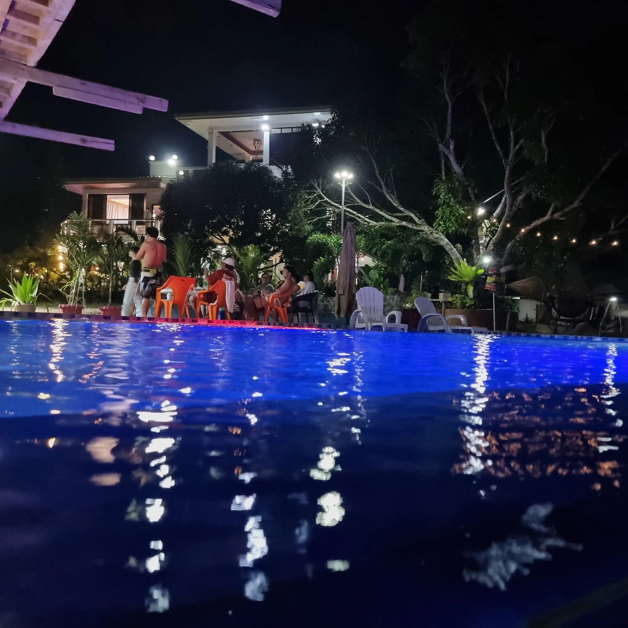 The infinity pool lit blue at night during a party, with guests at the poolside tables